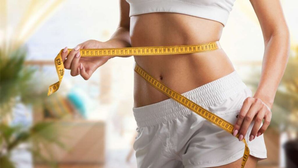 Eine Frau misst ihren Bauchumfang, um Messwerte für die Gewichtsabnahme zu bekommen.