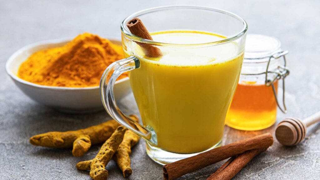 Ein Glas goldene Milch auf einem Holztisch. Die goldene Milch ist ein beliebtes Getränk in der ayurvedischen Ernährung und enthält Kurkuma und andere Gewürze, die zur Förderung von Gesundheit und Wohlbefinden beitragen können
