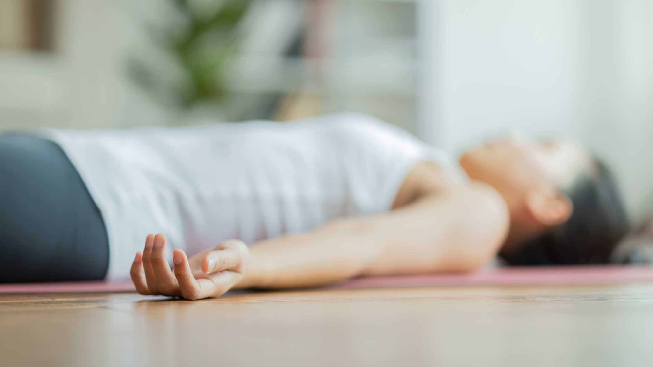 Eine Frau liegt auf dem Rücken und entspannt vollständig. Die Augen geschlossen und der Atem ist tief und gleichmäßig. Sie befindet sich in einer Yoga Nidra Position und lässt alle Anspannungen und Sorgen los.