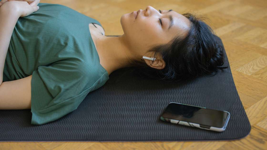 Eine Frau entspannt auf ihrer Yogamatte und genießt ihr NSDR (Non Sleep Deep Rest).