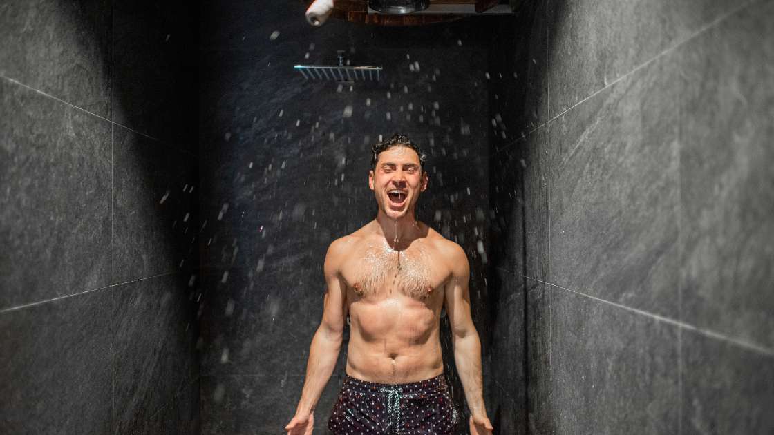 Ein fröhlicher Mann in Badehose unter einer kalten Dusche